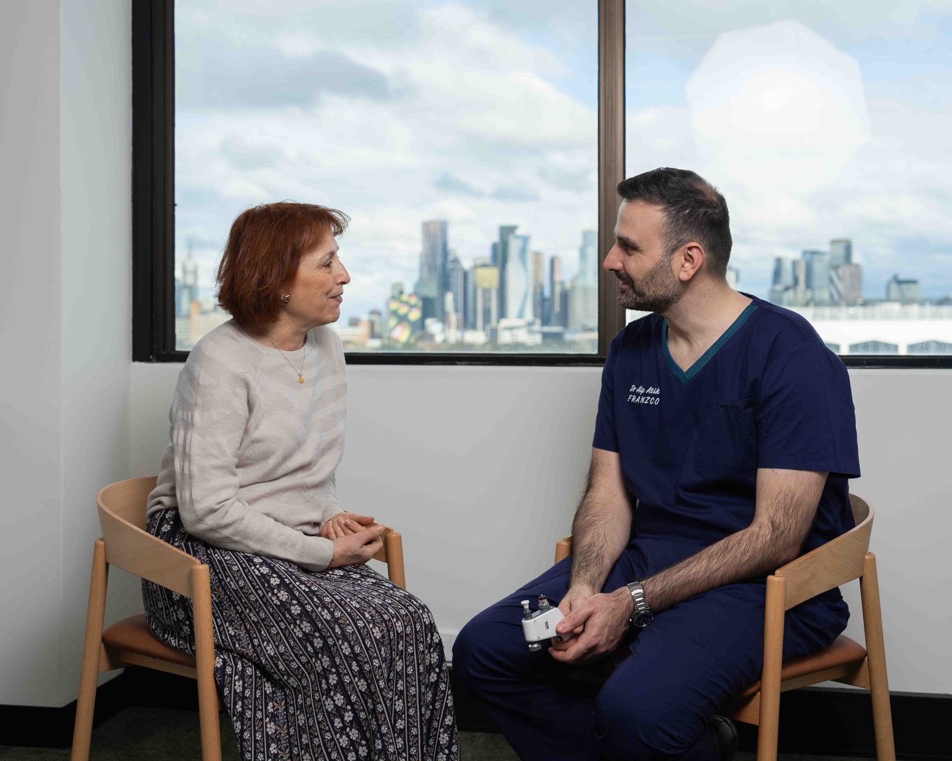 Dr Alp Atik mid-consultation with the Melbourne skyline behind him